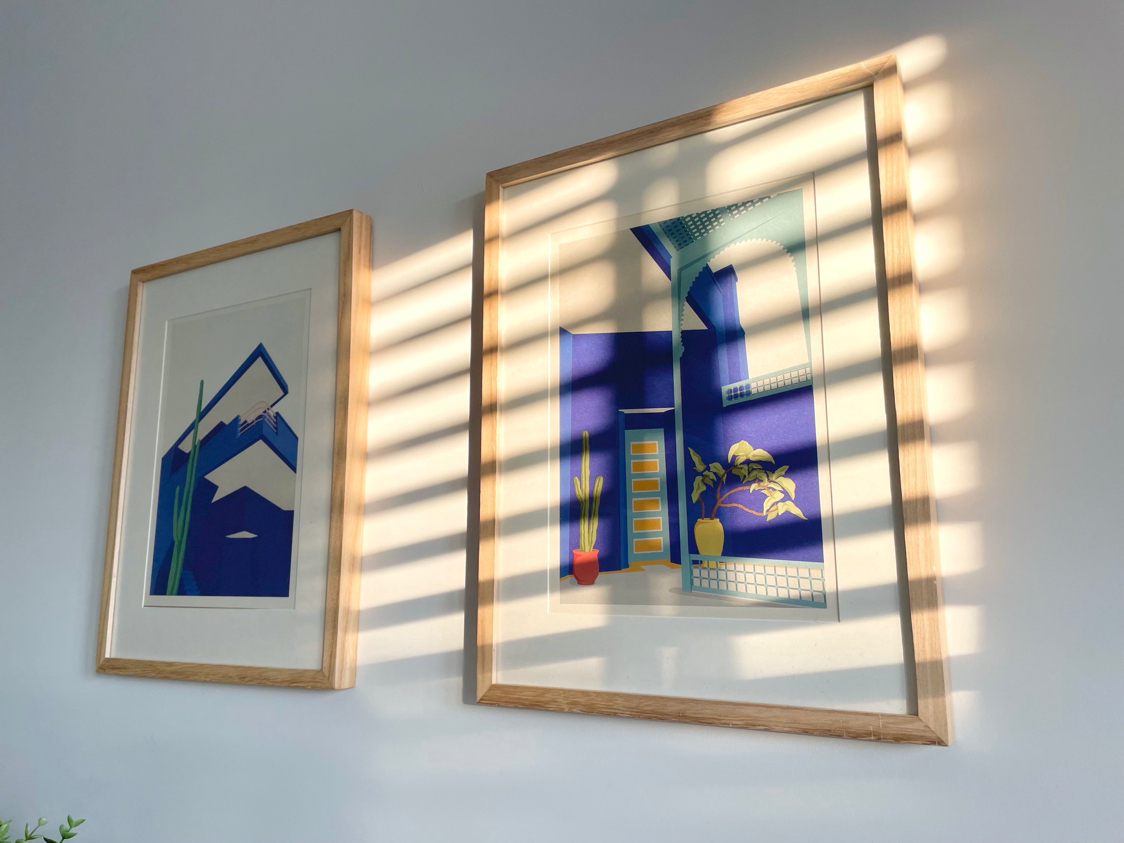 Two framed artworks on a wall with sunlight casting shadows.